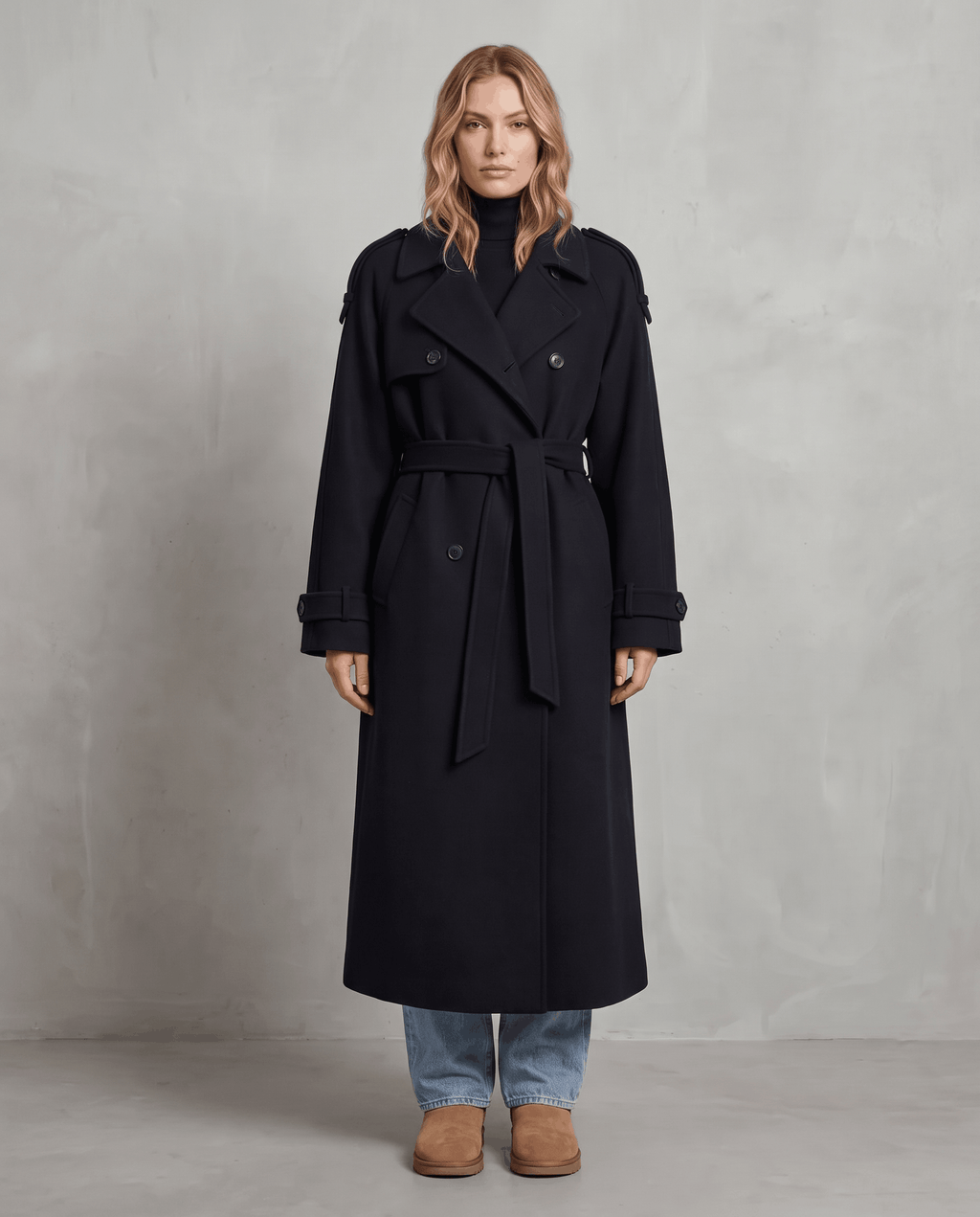 Black wool trench coat in an oversized, longline silhouette with a double-breasted front and belted waist.