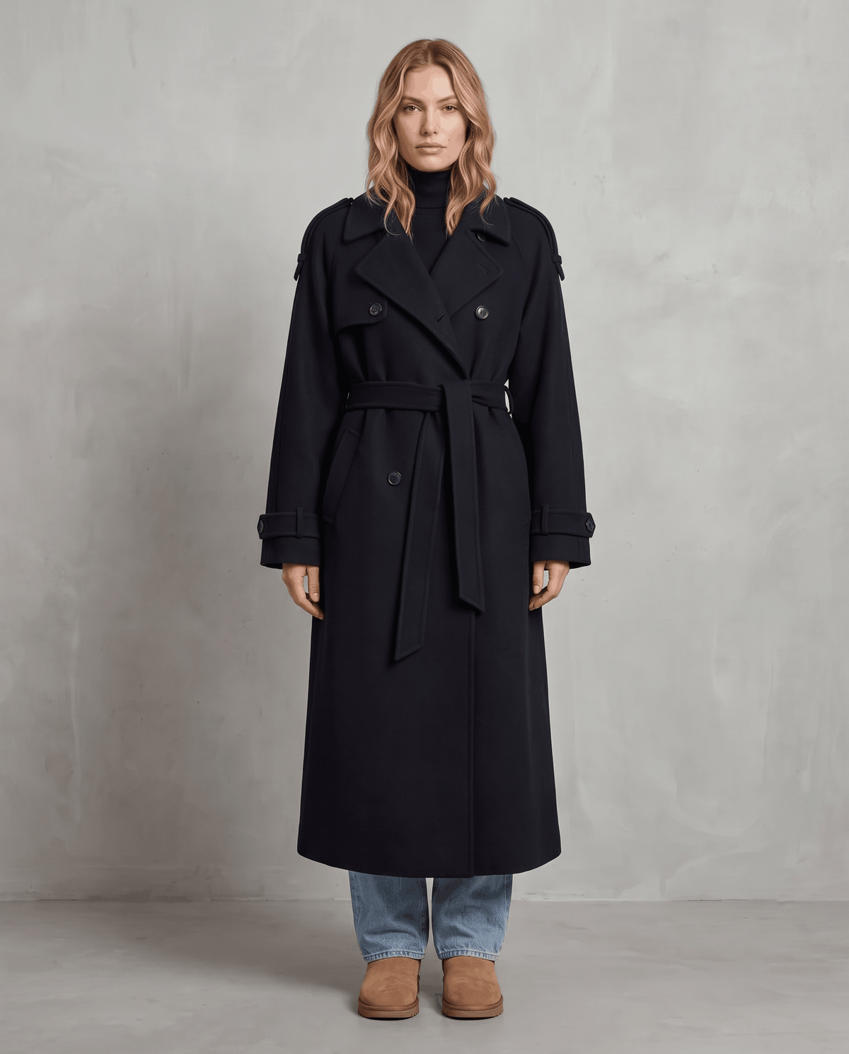 Black wool trench coat in an oversized, longline silhouette with a double-breasted front and belted waist.