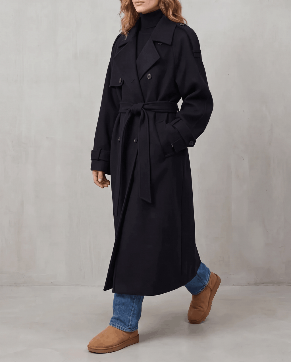 Black wool trench coat in an oversized, longline fit with a double-breasted front and belted waist.