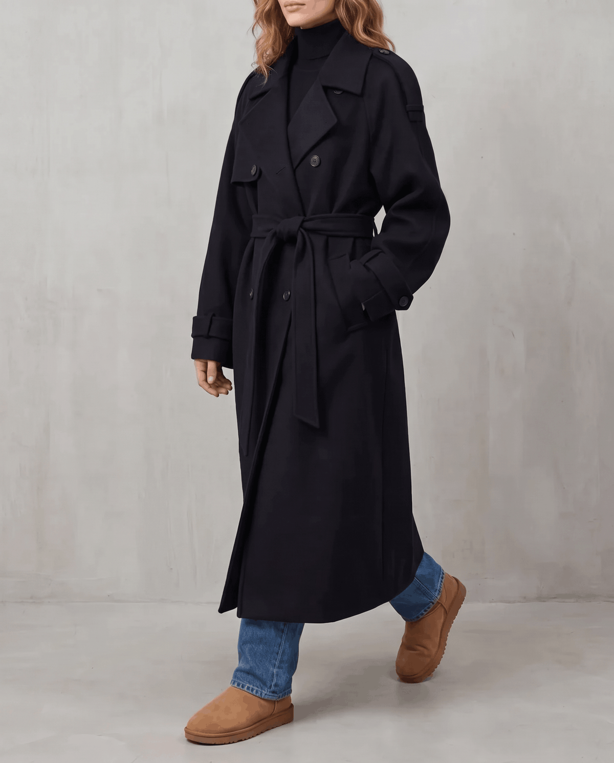 Black wool trench coat in an oversized, longline fit with a double-breasted front and belted waist.