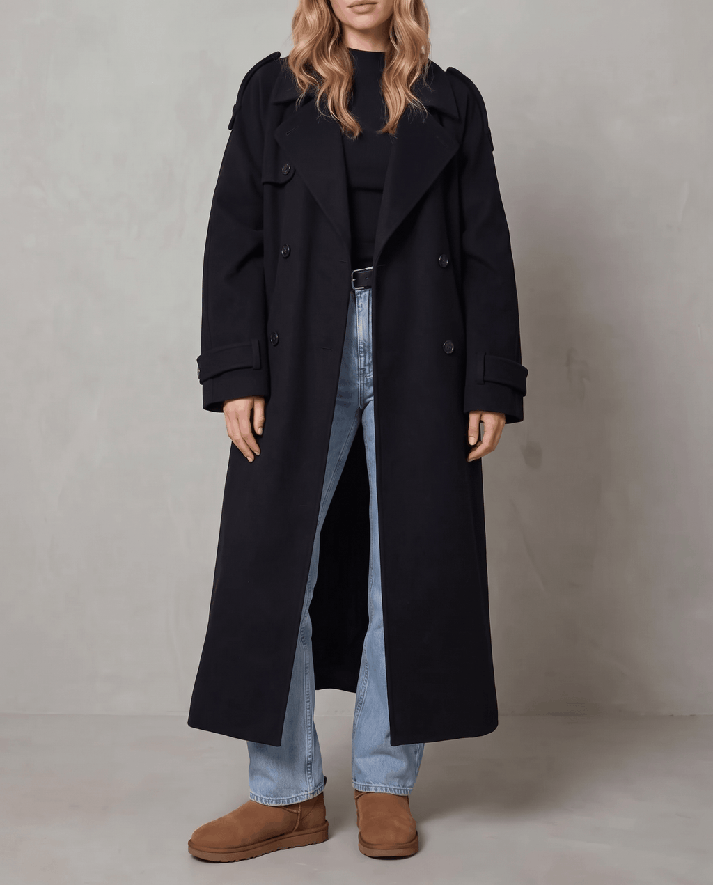 Black wool trench coat in an oversized, longline silhouette with a double-breasted front and belted waist.