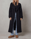 Black wool trench coat in an oversized, longline silhouette with a double-breasted front and belted waist.