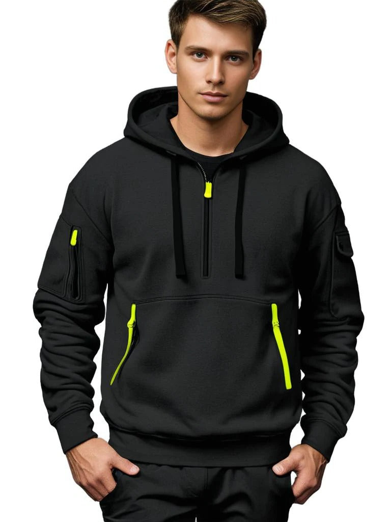 Man wearing a black tactical hoodie featuring an adjustable hood, half-zip neckline, and contrast zipper accents.