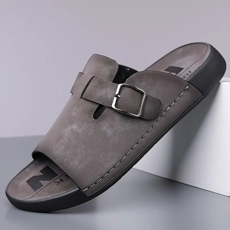 Gray vegan leather slide sandal with an adjustable buckle strap and textured footbed, angled on a white display block.