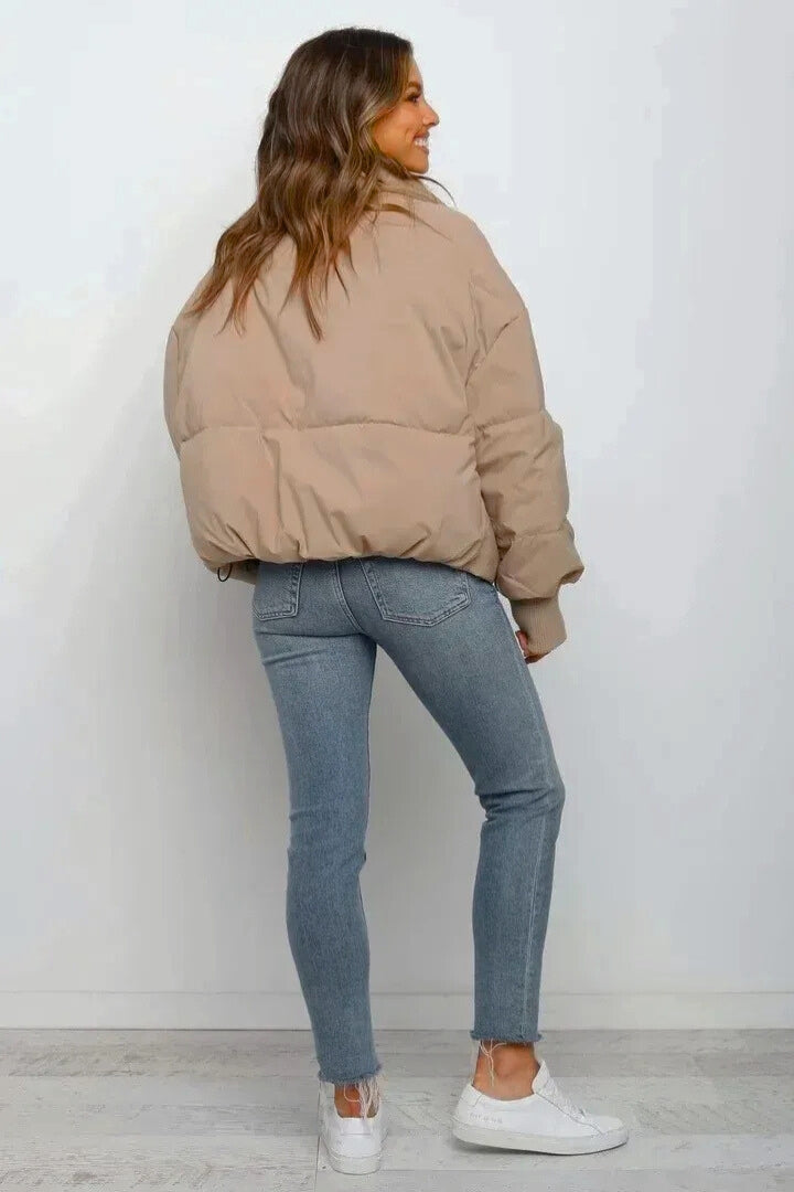 Beige cropped quilted puffer jacket with a relaxed fit, worn over blue denim jeans and white sneakers.