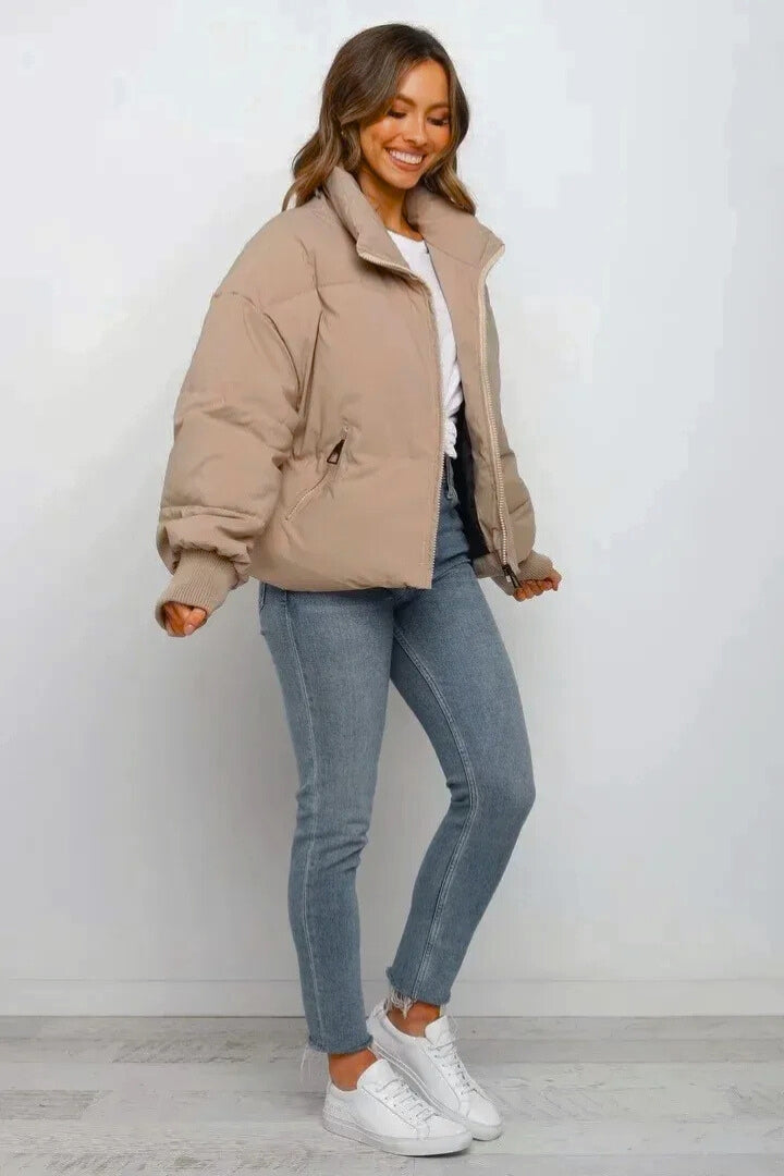 Beige cropped quilted puffer jacket with a full zip front, ribbed cuffs, and a relaxed fit worn over blue jeans.