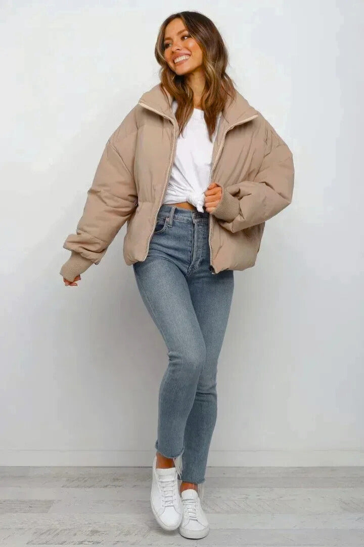 Beige cropped quilted puffer jacket with a full zip front, ribbed cuffs, and a relaxed fit worn over blue jeans.