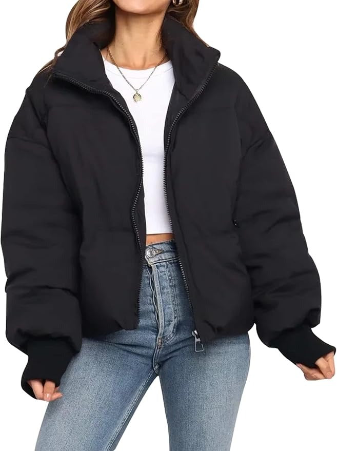 Black cropped puffer jacket with quilted padding, full zip front, and ribbed cuffs worn over a white top and blue jeans.