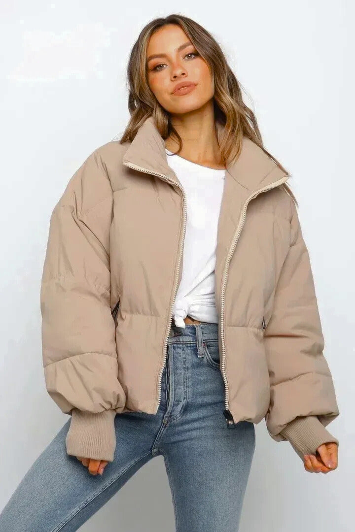 Beige cropped puffer jacket with quilted padding, full zip front, and ribbed cuffs worn over a white tee and denim jeans.