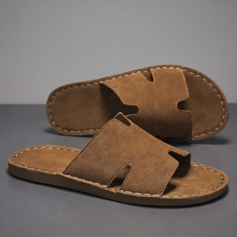Pair of brown suede slide sandals with H-shaped cutout straps stacked on a gray backdrop