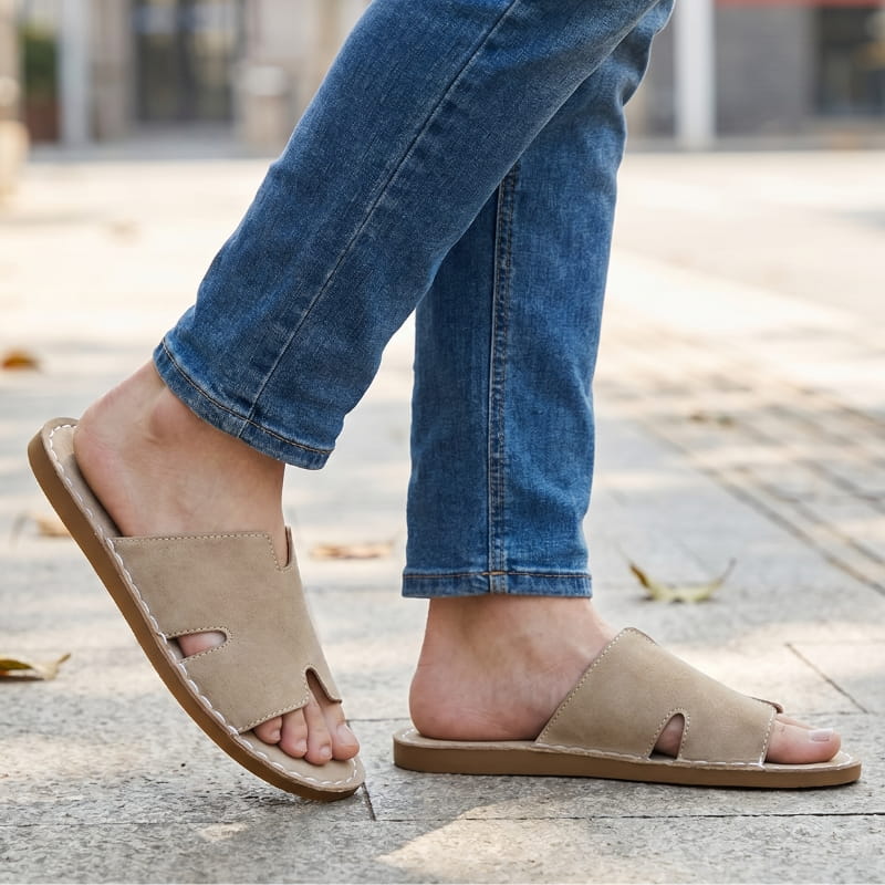 Legs in cropped jeans wearing khaki suede slide sandals, mid-stride on an outdoor stone plaza