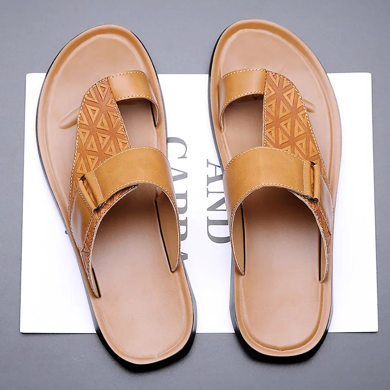 Overhead view of a pair of khaki leather sandals with geometric-textured toe-loop straps, resting on branded paper packaging.