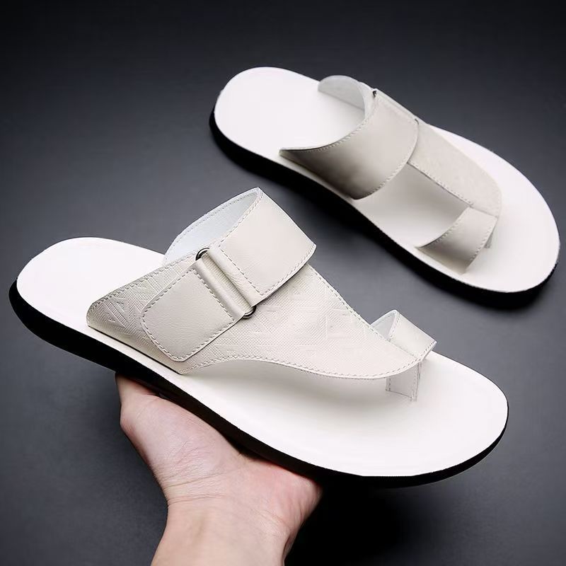 Hand holding a pair of white leather sandals with buckle straps against a dark background.