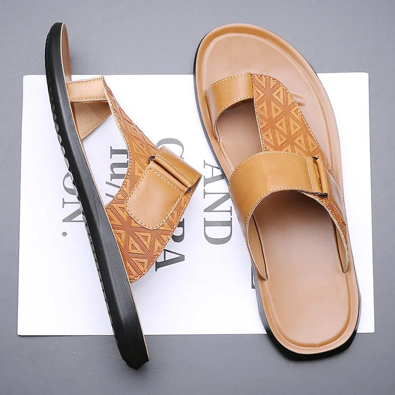 Tilted overhead view of a pair of khaki leather sandals with geometric-textured toe-loop straps, resting on branded paper packaging.