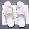 Overhead view of a pair of white leather geometric-texture sandals with toe-loop straps, resting on branded paper packaging.