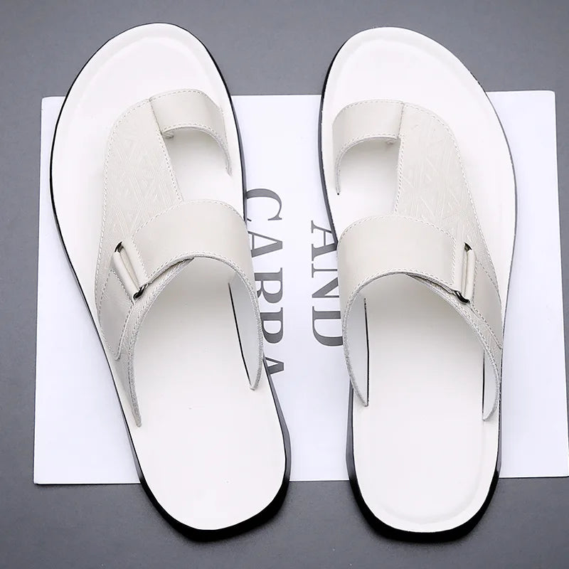 Overhead view of a pair of white leather geometric-texture sandals with toe-loop straps, resting on branded paper packaging.