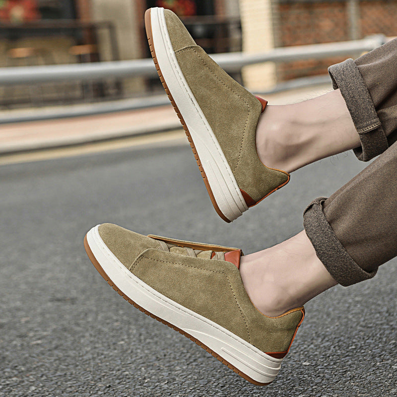 Close-up of feet wearing olive suede Dominic slip-on sneakers, mid-stride on a city street with cuffed pants