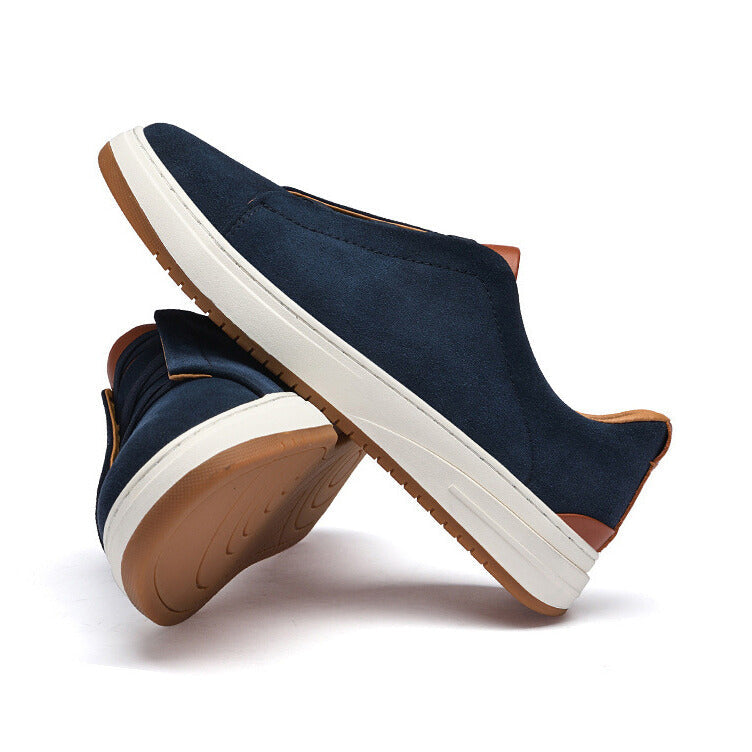 Pair of navy blue suede Dominic slip-on sneakers stacked at an angle showing the tan tread sole, on a plain white background