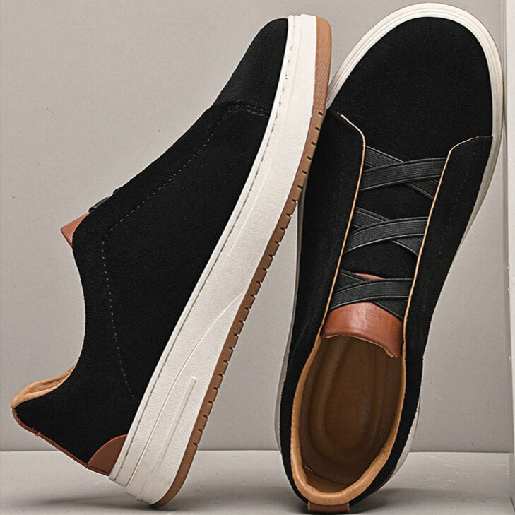 Two black suede Dominic slip-on sneakers propped against each other, one showing the tan interior lining and sole