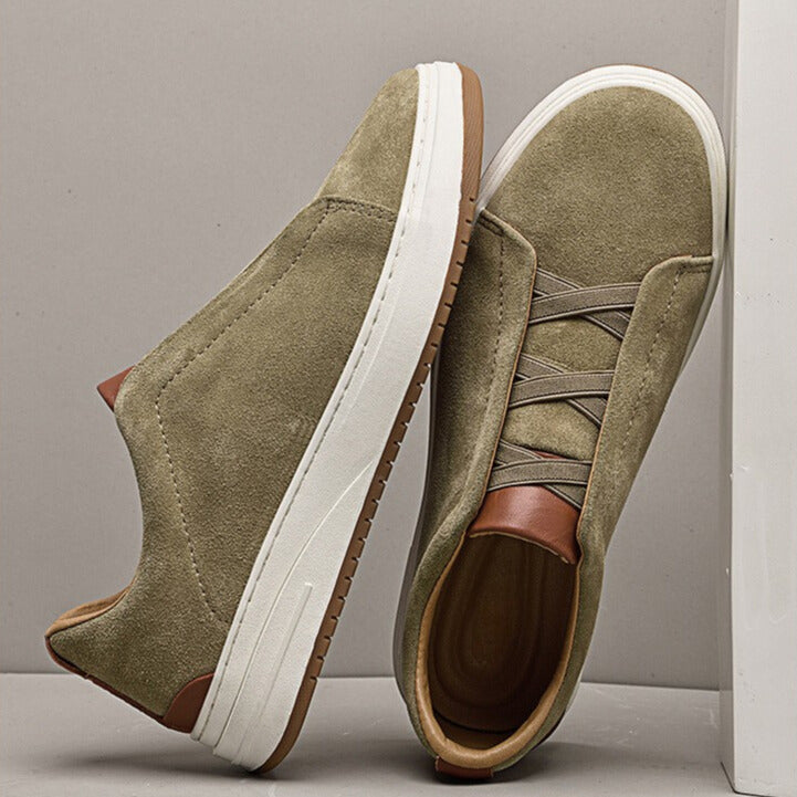 Two olive suede Dominic slip-on sneakers propped against each other, one showing the tan interior lining and sole