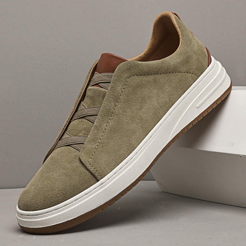 Single olive suede Dominic slip-on sneaker with elastic gore lacing and white sole, leaning against a white box