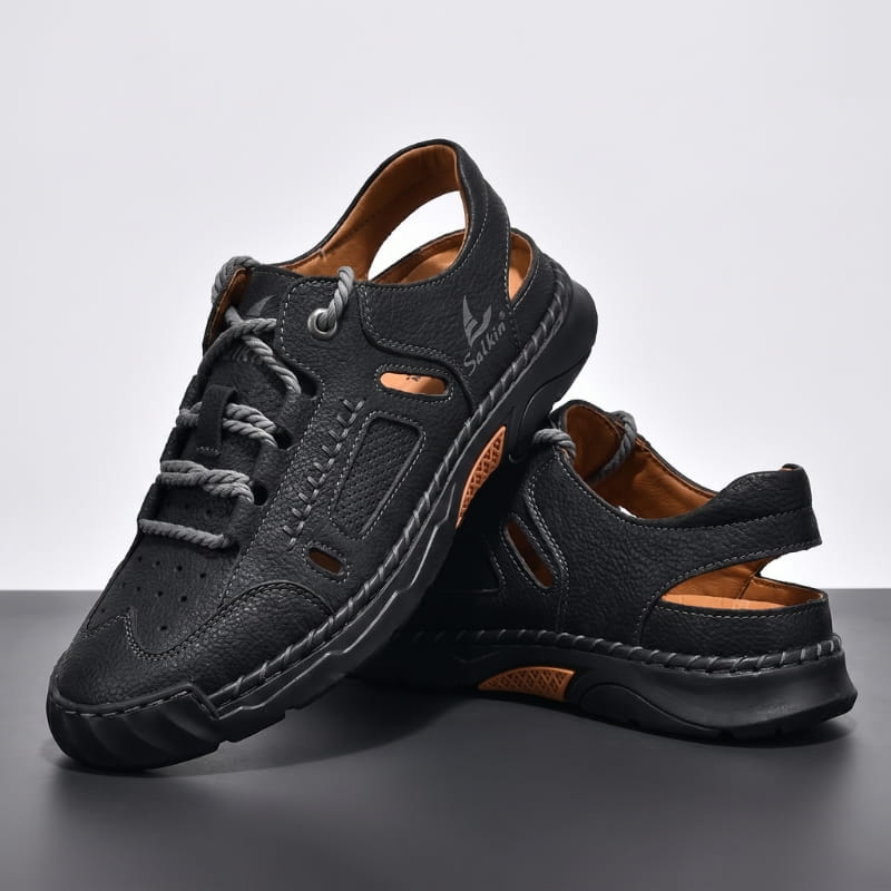 Pair of black leather fisherman sandals with orange trim stacked on a dark studio backdrop