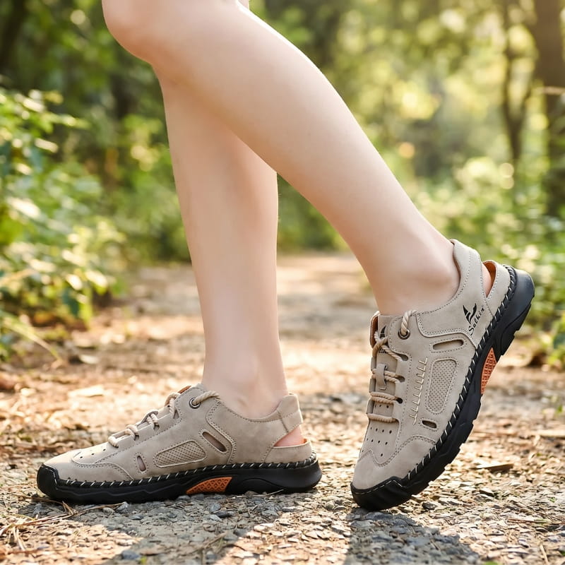 Bare ankles wearing khaki nubuck fisherman sandals, walking on a sunlit gravel path through a wooded area