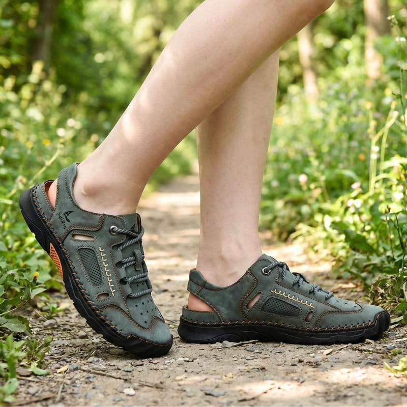 Bare ankles wearing green nubuck fisherman sandals, walking on a lush wooded trail