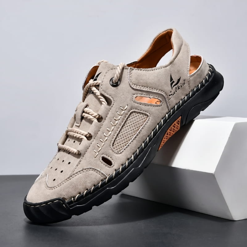 Khaki nubuck leather fisherman sandal with rope-style laces and perforated panels propped diagonally against a white geometric block