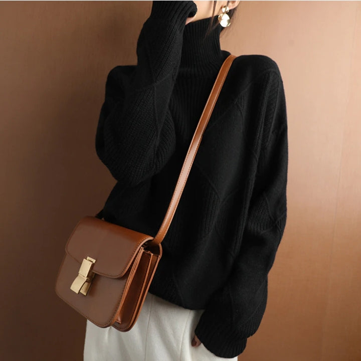 Woman wearing a black ribbed turtleneck knit sweater with long sleeves and a relaxed fit, styled with a crossbody bag.