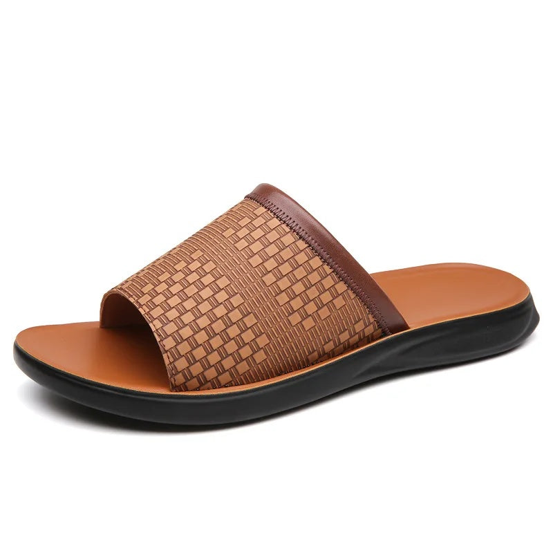 Side profile product shot of a tan woven-texture leather slide sandal on a plain white background, showing the dark brown trim strap and molded footbed.