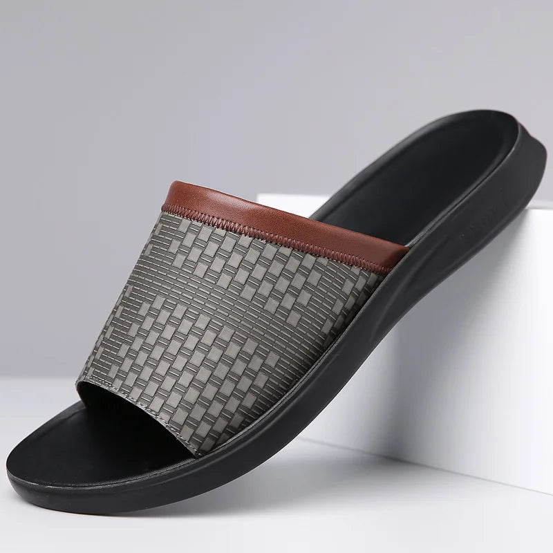 Gray woven-texture leather slide sandal with a brown leather trim strap and molded black sole, angled on a white display block.