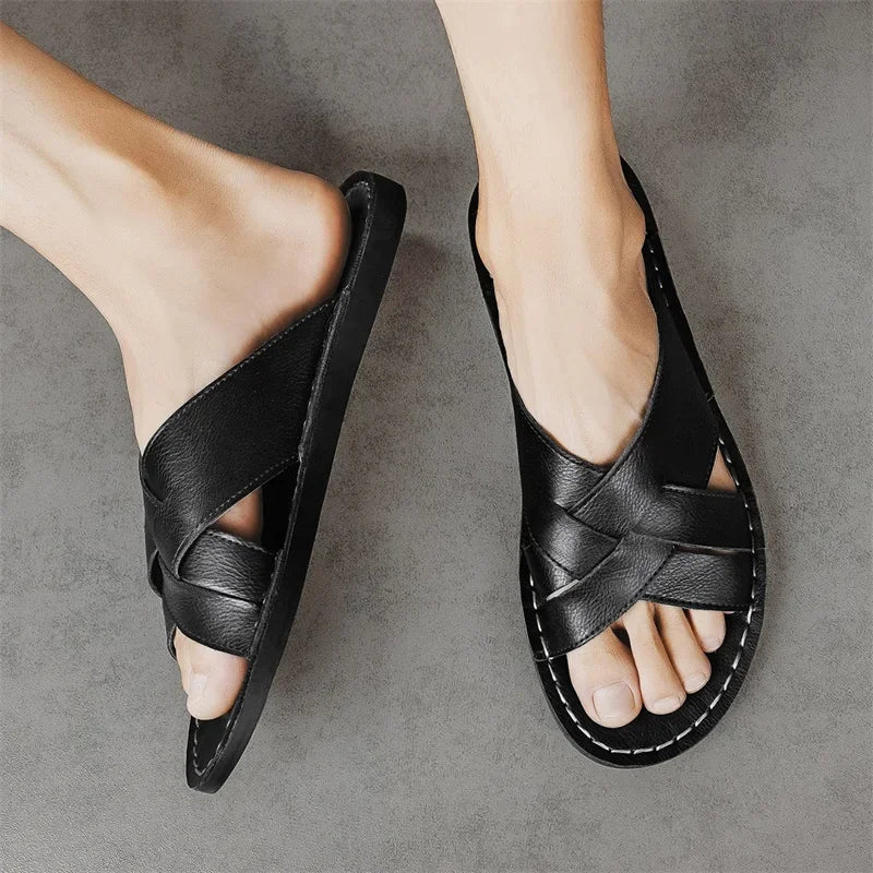 Overhead view of a model's feet wearing a pair of black woven leather cross-strap sandals against a gray background.