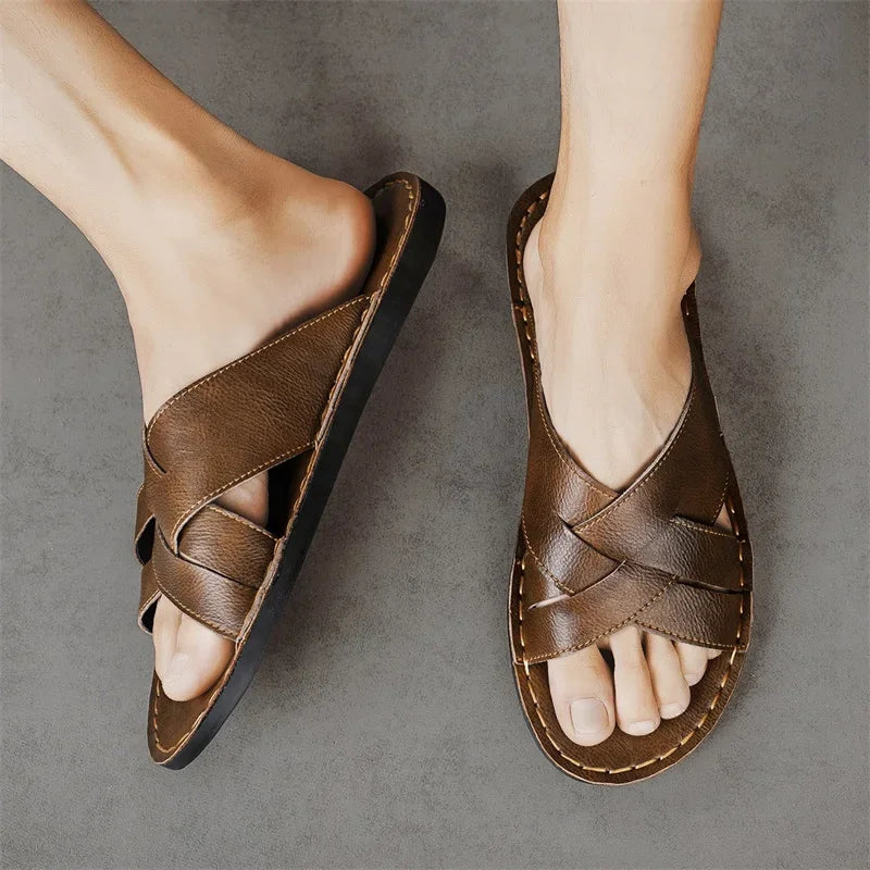 Overhead view of a model's feet wearing a pair of brown woven leather cross-strap sandals against a gray background.