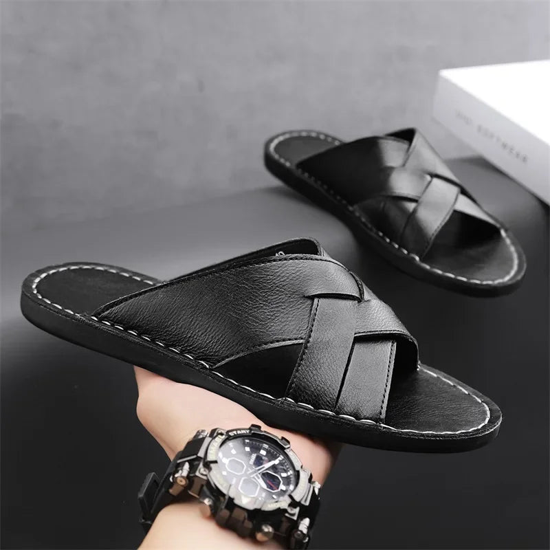 Pair of black woven leather cross-strap sandals balanced on a person's wrist wearing a watch, styled as a lifestyle product shot.