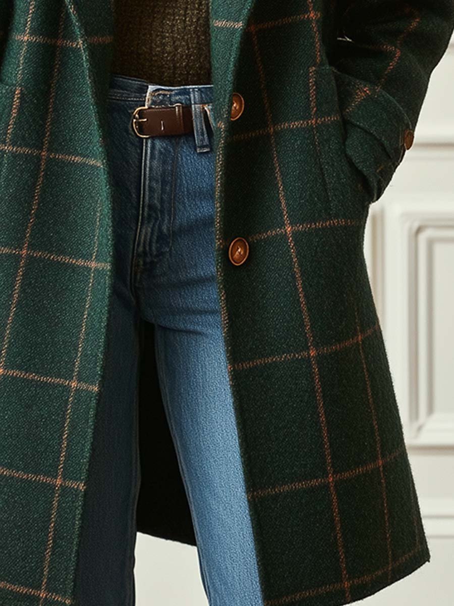 Close-up of a dark green plaid long coat showing the textured plaid fabric, button closure, and front pocket detail.