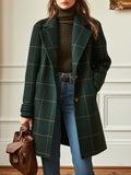 Woman wearing a dark green plaid long coat with a notched lapel, button-front closure, and relaxed tailored fit over a brown turtleneck sweater and blue jeans.