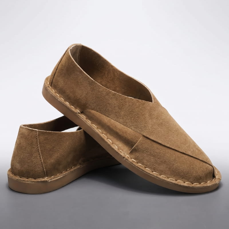 Pair of brown suede slip-on sandals with cross-wrap cutout design stacked on a gray backdrop