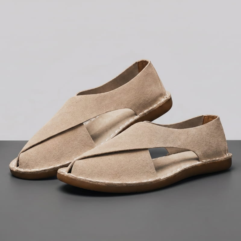 Pair of khaki suede slip-on sandals with cross-wrap cutout design on a gray studio floor