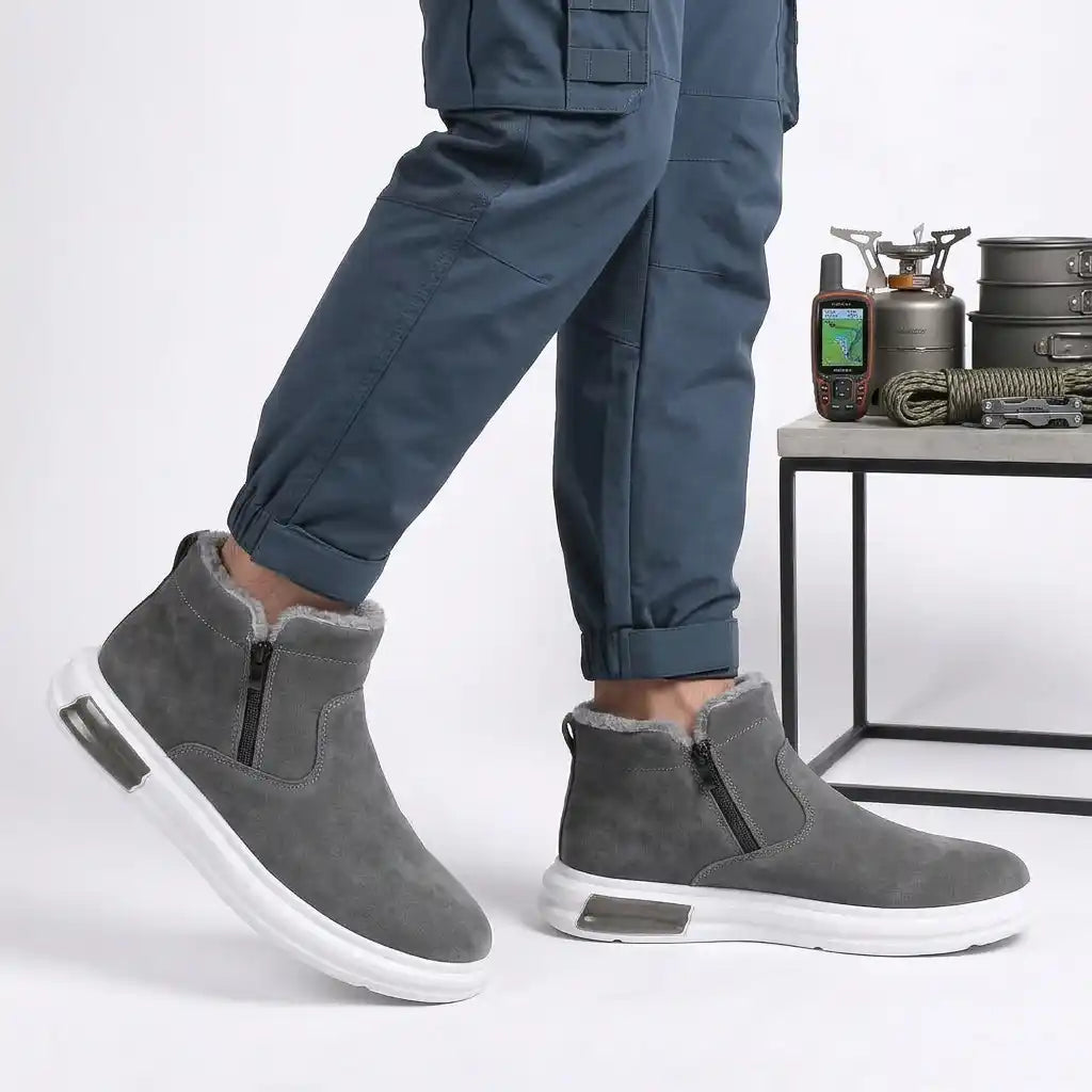 Gray fur-lined winter boots for men worn by a person, featuring a wide toe box, side zip, and cushioned sole