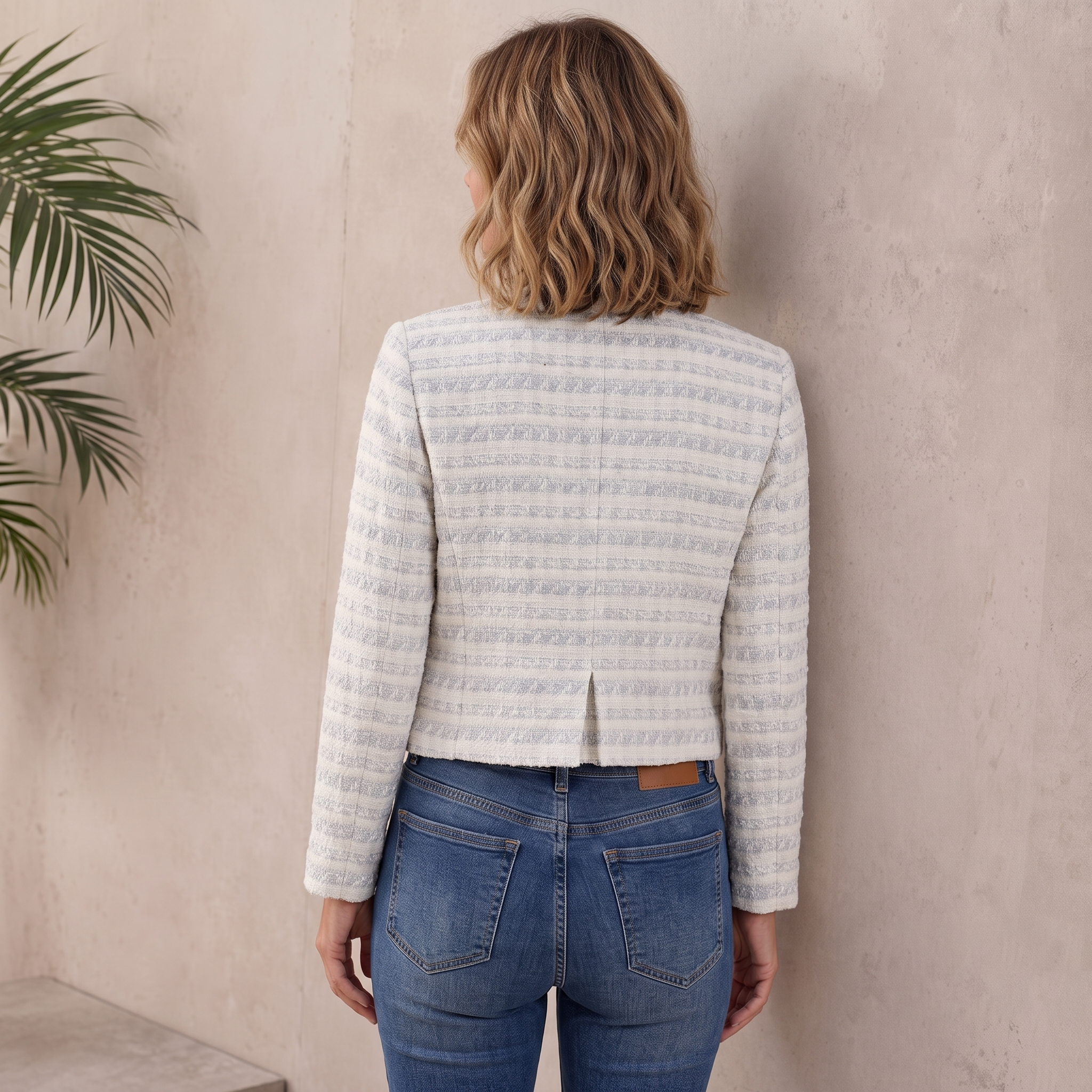 Back view of a woman wearing a light gray textured tweed jacket with a fitted silhouette and long sleeves.