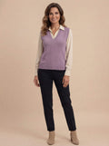 Woman wearing a purple knit sweater vest with a V-neck and sleeveless design layered over a cream button-up shirt, paired with black trousers and ankle boots.