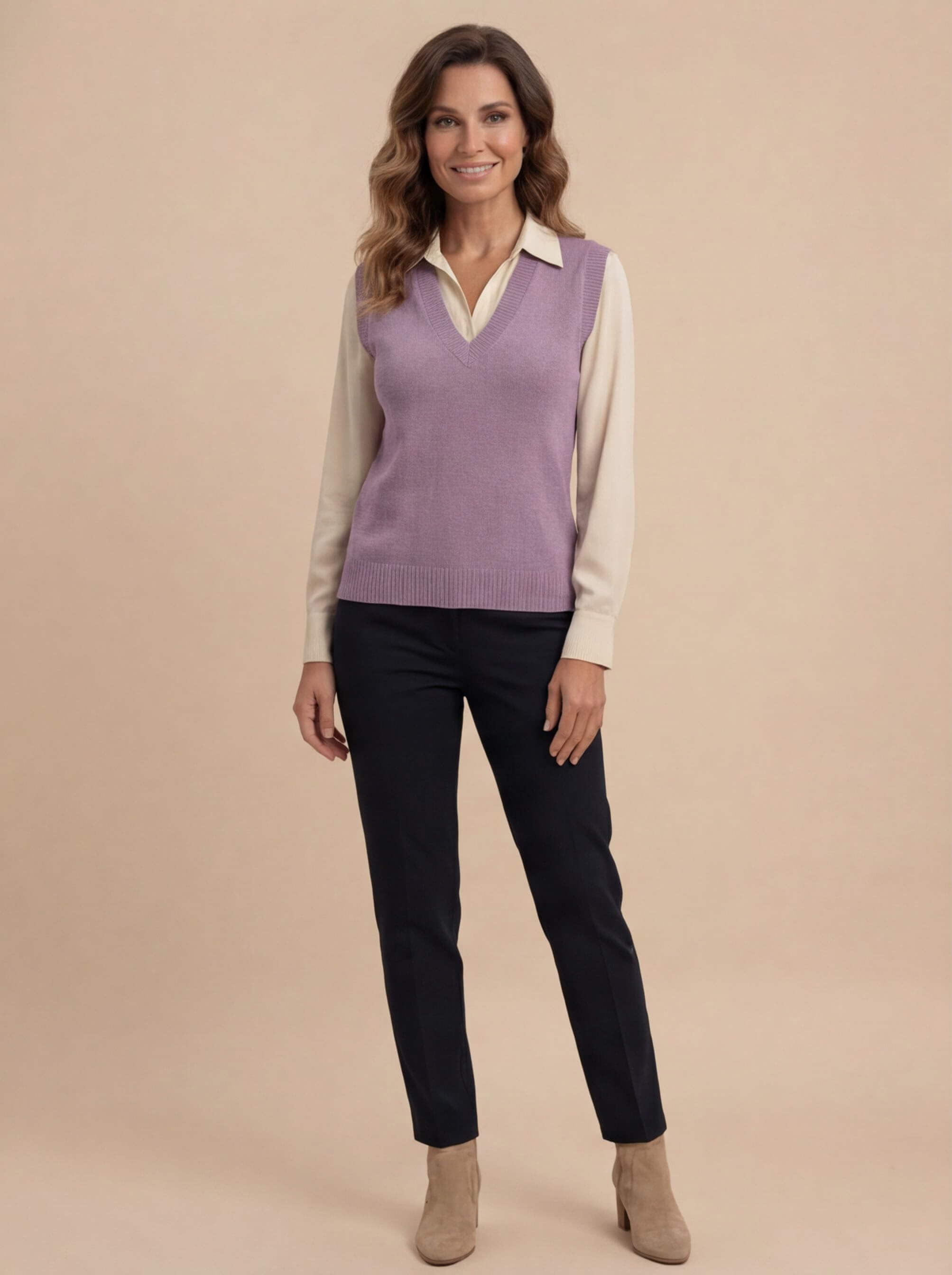 Woman wearing a purple knit sweater vest with a V-neck and sleeveless design layered over a cream button-up shirt, paired with black trousers and ankle boots.