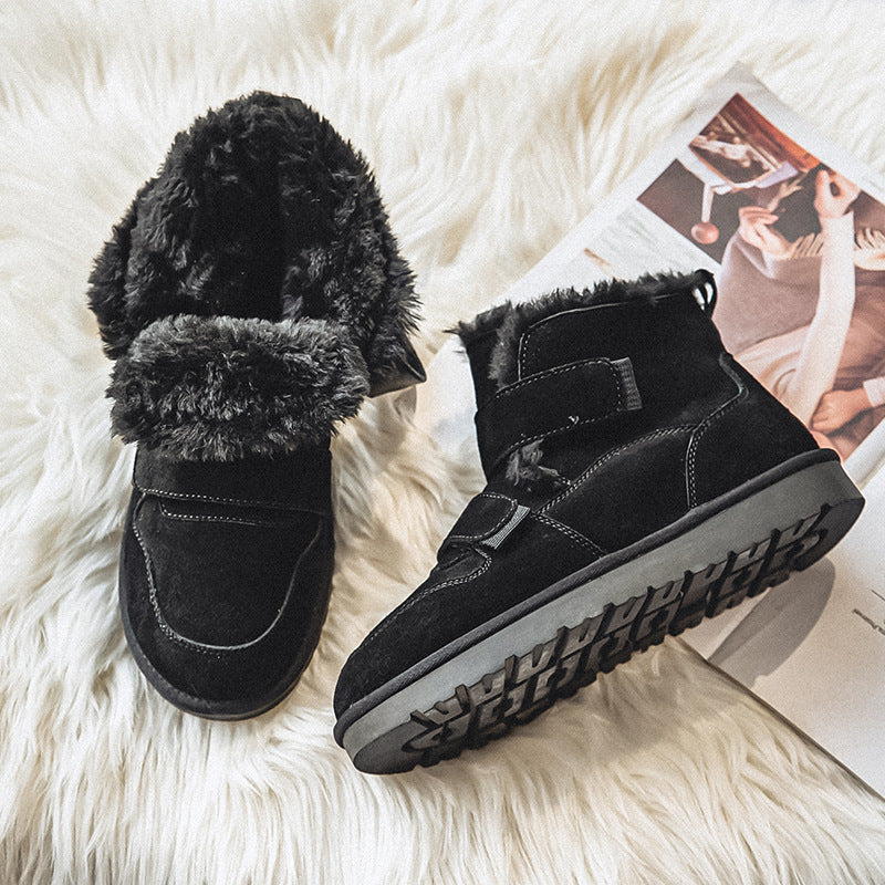 Pair of black suede fleece-lined winter boots with velcro strap closures, resting on a faux fur rug beside a magazine.