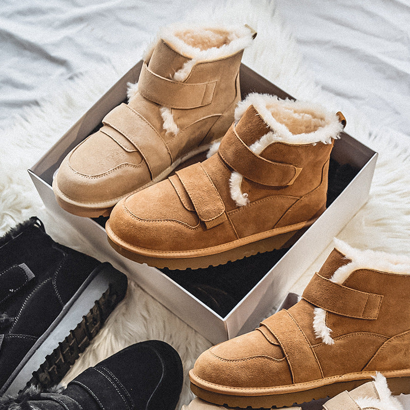 Close-up of tan suede fleece-lined winter boots in an open shoe box, with a black pair visible in the background, on a faux fur rug.