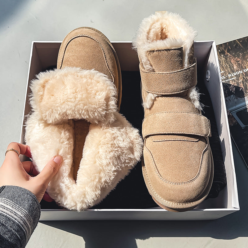 A hand reaching into an open shoe box holding a tan suede fleece-lined winter boot, outdoors on a sunny day.