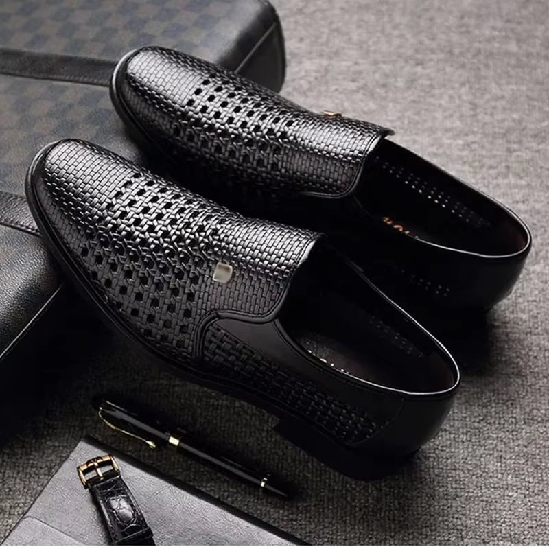 Pair of black woven calfskin leather loafers with breathable perforated detailing and flexible black soles, displayed alongside a leather wallet and pen.