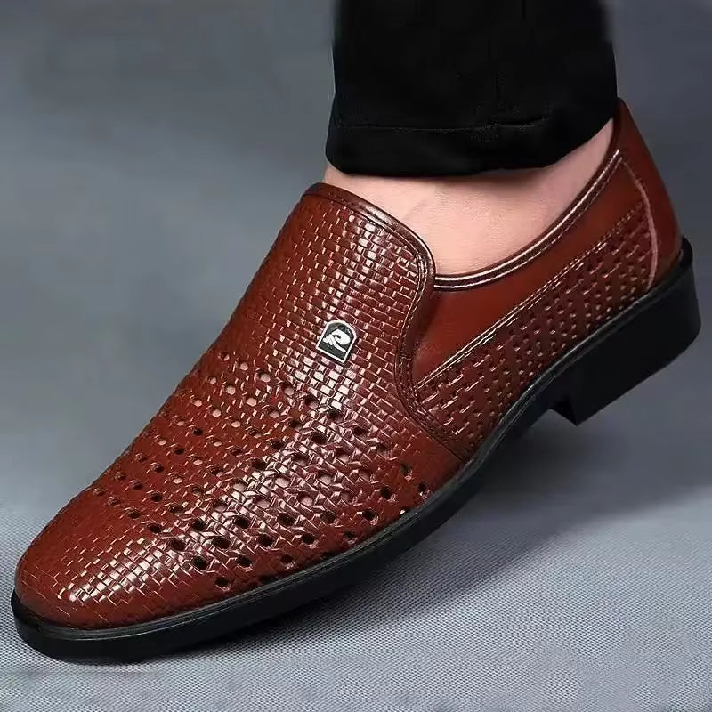 Brown woven calfskin leather loafers with breathable perforated detailing and a flexible black sole, worn with black trousers in a modern indoor setting.