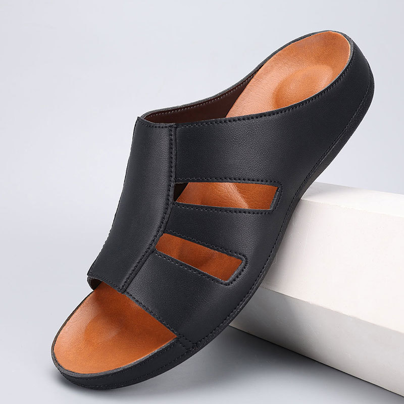 Black leather slip-on sandal with cutout strap detailing and an orange-toned footbed, angled on a white display block.