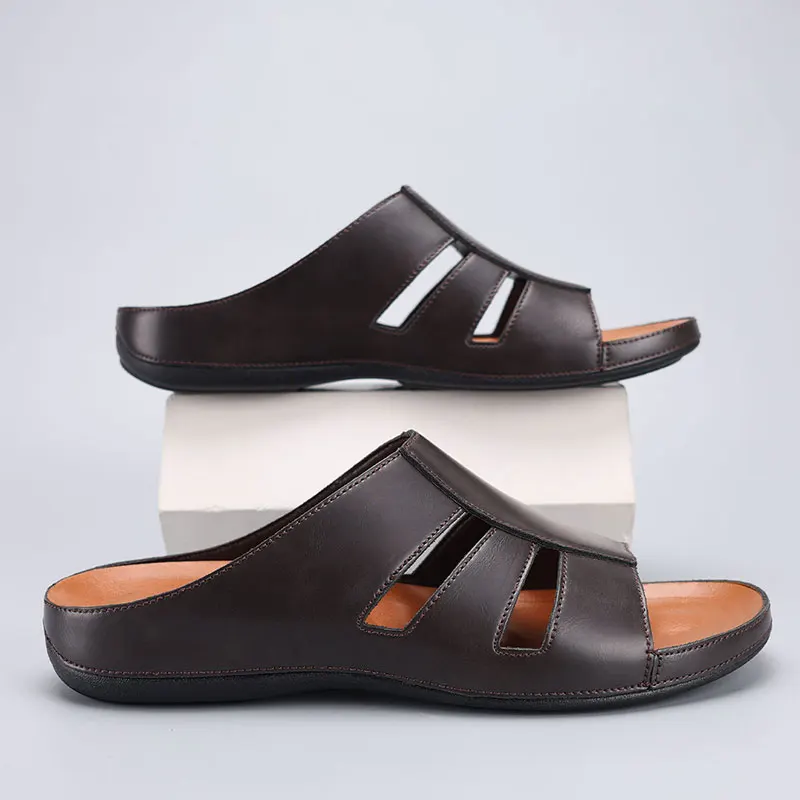 Pair of black leather slip-on sandals with cutout straps, one shoe stacked on a white display block above the other.
